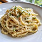 A close-up of a serving of creamy lemon pasta, generously topped with grated Parmesan cheese and fresh parsley.
