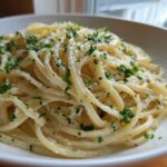 A close-up view of a serving of creamy lemon pasta tossed in a light sauce, topped with grated cheese and fresh chopped parsley.