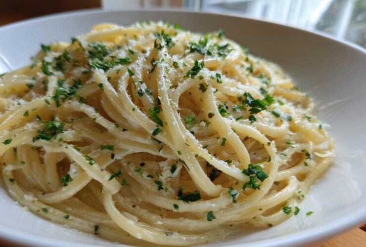A close-up view of a serving of creamy lemon pasta tossed in a light sauce, topped with grated cheese and fresh chopped parsley.