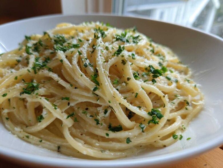 A close-up view of a serving of creamy lemon pasta tossed in a light sauce, topped with grated cheese and fresh chopped parsley.