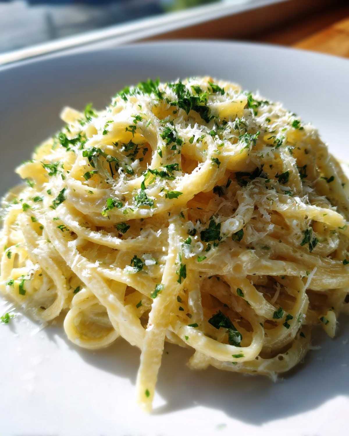 A close-up shot of a serving of creamy lemon pasta topped generously with grated Parmesan cheese and fresh chopped parsley.
