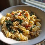 A close-up of creamy marry me chicken pasta featuring fusilli noodles, spinach, and sun-dried tomatoes in a white bowl.