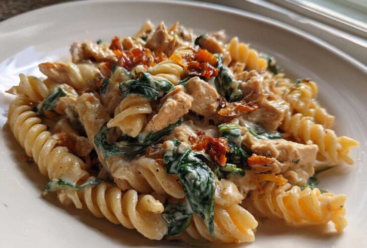 Close-up of creamy marry me chicken pasta featuring fusilli, chicken pieces, spinach, and sun-dried tomatoes on a white plate.