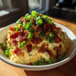 A bowl of creamy Million Dollar Dip generously topped with crumbled bacon and fresh green onions.