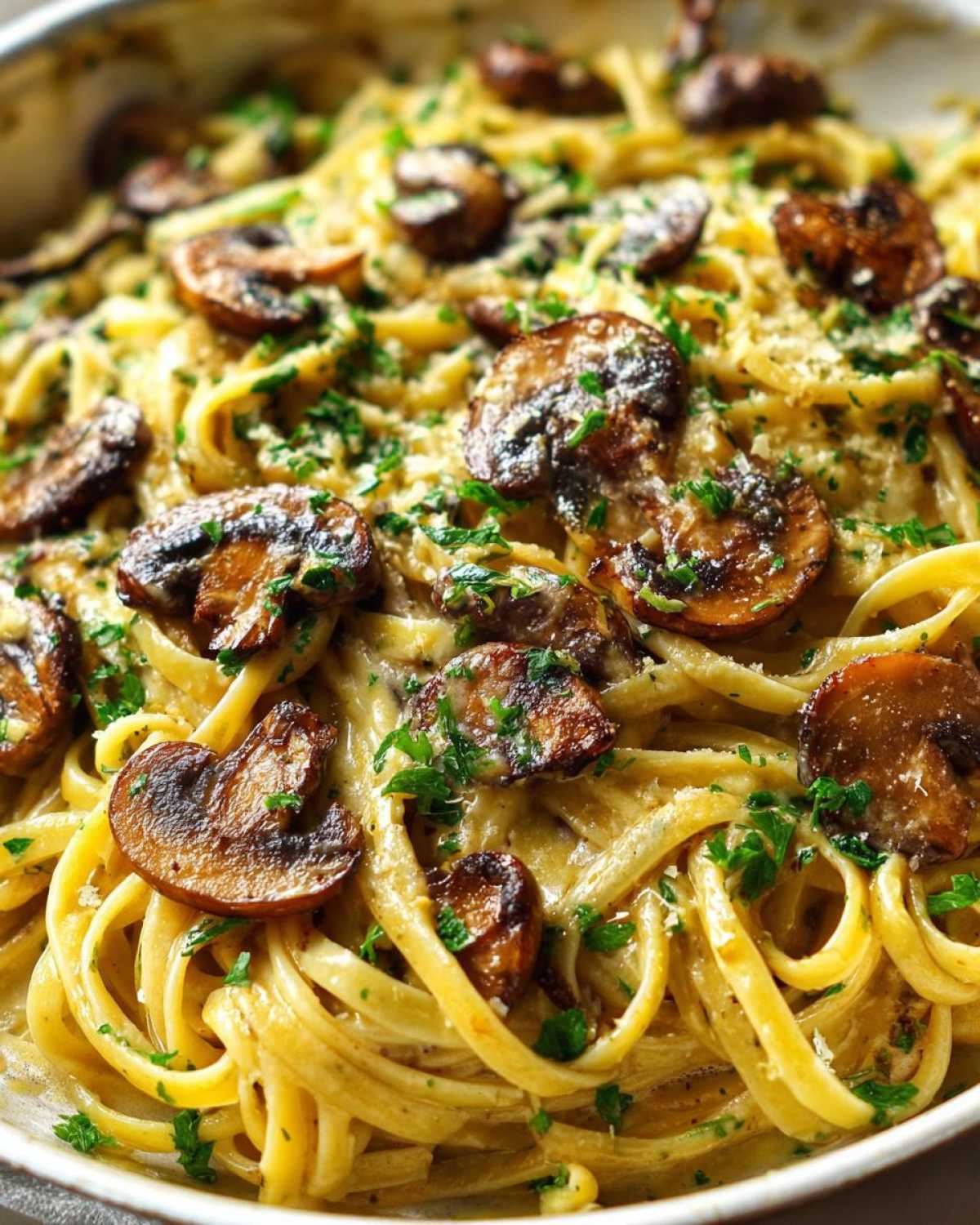 A close-up, overhead view of creamy mushroom pasta featuring linguine coated in a rich sauce, topped with sautéed mushrooms and fresh parsley.