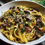 Close-up of creamy fettuccine mushroom pasta topped with sautéed mushrooms and fresh parsley.