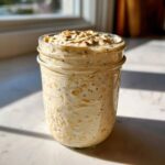 A jar filled with creamy overnight oats mixed with chia seeds and topped with rolled oats.
