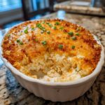 A close-up of a hot, creamy popper dip in a white baking dish with a golden, cheesy crust and green onion garnish.