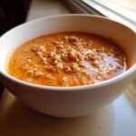 Close-up of a creamy, orange-hued pumpkin chili with ground meat served in a white bowl.
