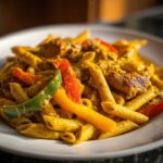 A close-up, appetizing shot of creamy Rasta Pasta featuring penne, chicken pieces, and vibrant red, yellow, and green bell peppers.