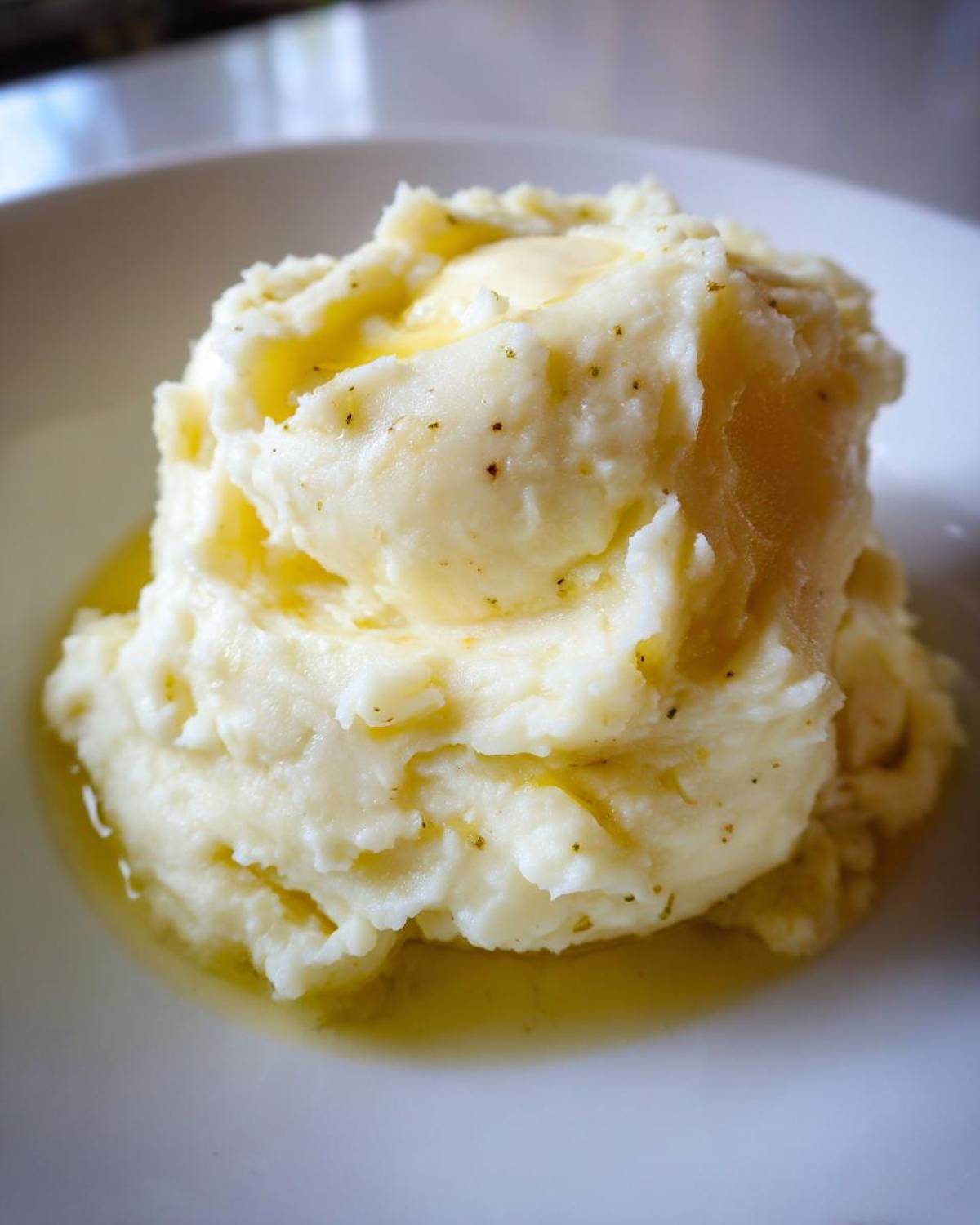 A close-up of creamy roasted garlic mashed potatoes topped with melting butter in a white bowl.
