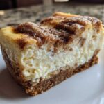 A thick slice of creamy snickerdoodle cheesecake featuring a graham cracker crust and a cinnamon sugar topping.