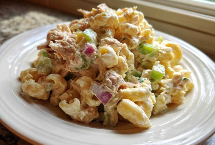 A generous serving of creamy Tuna pasta salad featuring elbow macaroni, tuna chunks, green celery, and red onion on a white plate.