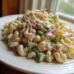 A close-up serving of creamy Tuna pasta salad made with elbow macaroni, celery, and red onion on a white plate.