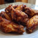 Close-up of several golden brown, crispy air fryer chicken wings piled on a white plate.