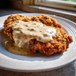 A golden brown, crispy chicken fried steak generously topped with creamy white pepper gravy.