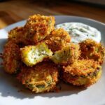 A pile of golden brown, crispy baked Fried Pickles served with a side of creamy white dipping sauce.