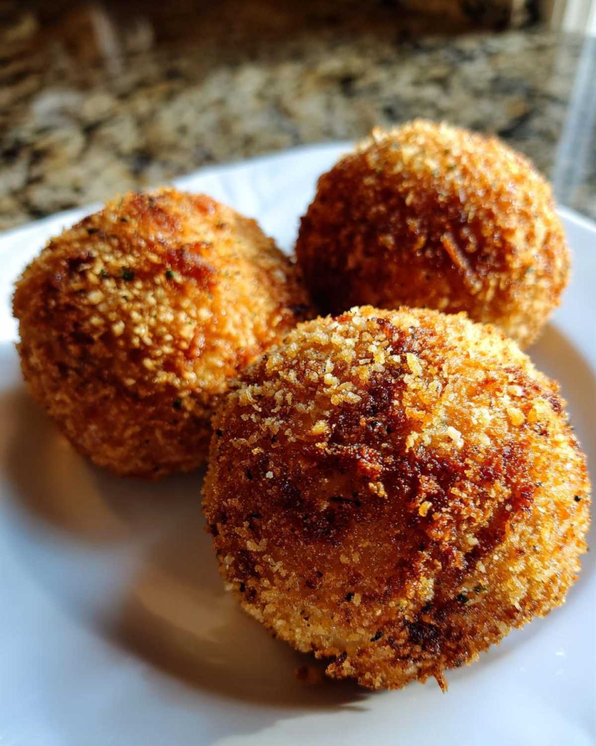 Three perfectly golden, crispy fried rice balls resting on a white plate, ready to eat.