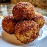 A stack of four golden brown, crispy fried rice balls served on a white plate.