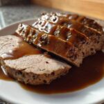 Close-up of sliced crockpot turkey breast covered in rich brown gravy on a white plate.