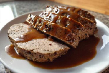 Close-up of sliced crockpot turkey breast covered in rich brown gravy on a white plate.