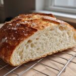 A close-up shot showing the airy crumb and golden, crusty top of a freshly baked french bread loaf resting on a wire cooling rack.