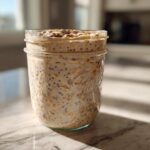 A close-up of creamy overnight oats mixed with chia seeds in a clear mason jar, ready to eat.