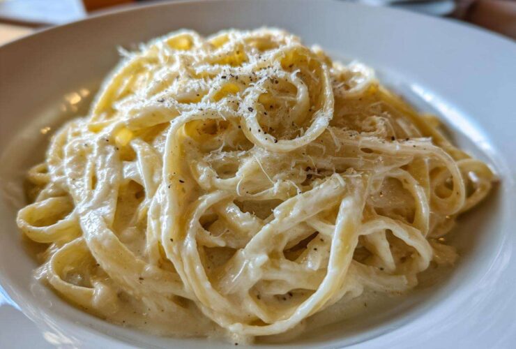 Close-up of fettuccine pasta generously coated in creamy homemade alfredo sauce and topped with grated cheese and black pepper.