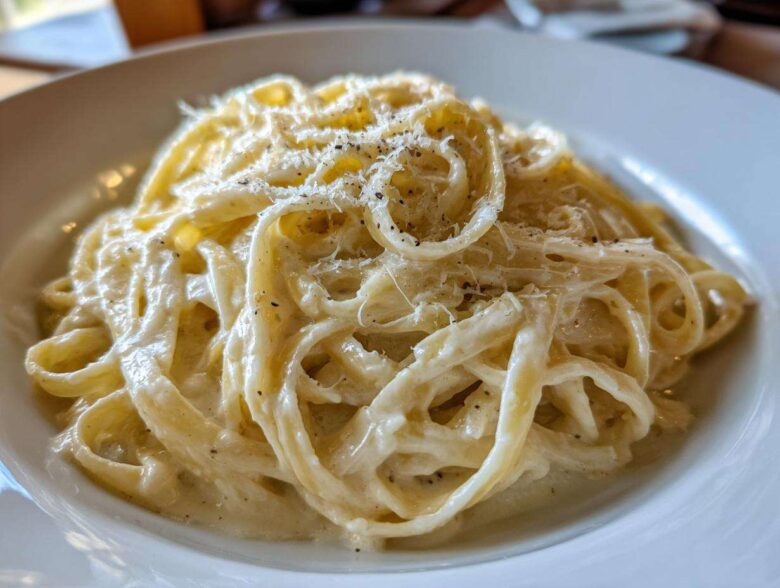 Close-up of fettuccine pasta generously coated in creamy homemade alfredo sauce and topped with grated cheese and black pepper.