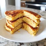 Close-up of a stack of fluffy coconut flour pancakes cut in half to show the interior texture.