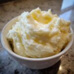 A close-up of creamy, fluffy mashed potatoes topped with melting butter in a white bowl.