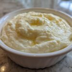 A close-up of creamy, fluffy mashed potatoes topped with melted butter served in a small white bowl.