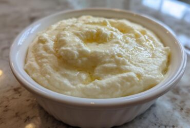 A close-up of creamy, fluffy mashed potatoes topped with melted butter served in a small white bowl.