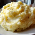 A close-up of a generous serving of fluffy roasted garlic mashed potatoes topped with melted butter and black pepper.
