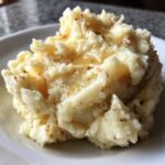 A close-up of fluffy roasted garlic mashed potatoes topped with melted butter and browned garlic bits.