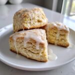 Three fluffy scones topped with a thick, dripping white glaze, served on a white plate.