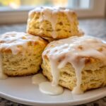 Three fluffy scones stacked slightly on a white plate, generously topped with dripping vanilla glaze.