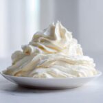 A large, fluffy swirl of creamy white vanilla buttercream frosting piled high in a small white bowl.