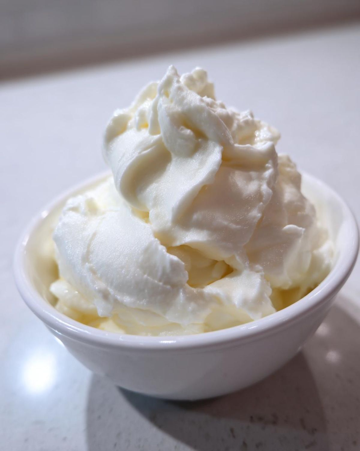A small white bowl filled with incredibly fluffy, creamy whipped topping, likely sour cream or butter, for perfect mashed potatoes.