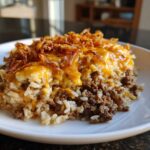 A close-up serving of french onion ground beef and rice casserole topped with melted cheddar cheese and crispy fried onions.