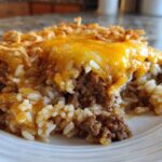 A close-up of a serving of french onion ground beef and rice casserole topped with melted cheddar cheese.