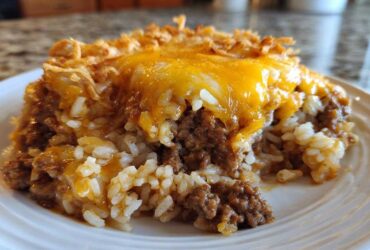 A close-up of a serving of french onion ground beef and rice casserole topped with melted cheddar cheese.