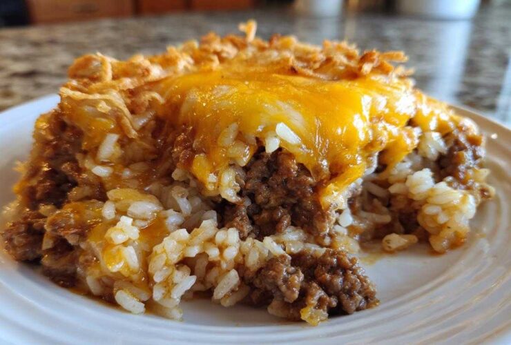 A close-up of a serving of french onion ground beef and rice casserole topped with melted cheddar cheese.