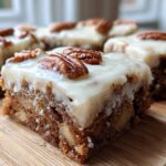 A close-up of a rich, fudgy apple brownies square topped with white frosting and a pecan half.