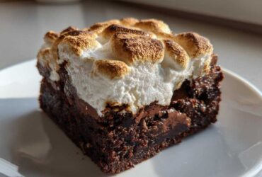 Close-up of a fudgy hot chocolate brownie slice topped with toasted, golden-brown marshmallows on a white plate.
