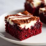 Close-up of a fudgy red velvet brownies square with a cream cheese swirl topping on a white plate.