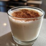 A creamy glass of homemade coquito recipe topped generously with ground cinnamon.