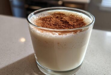A creamy glass of homemade coquito recipe topped generously with ground cinnamon.