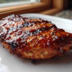 Close-up of a piece of grilled chicken heavily coated in shiny, dark homemade bbq sauce.