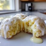 A soft lemon cookie, broken open to show the texture, dripping with thick white lemon glaze.